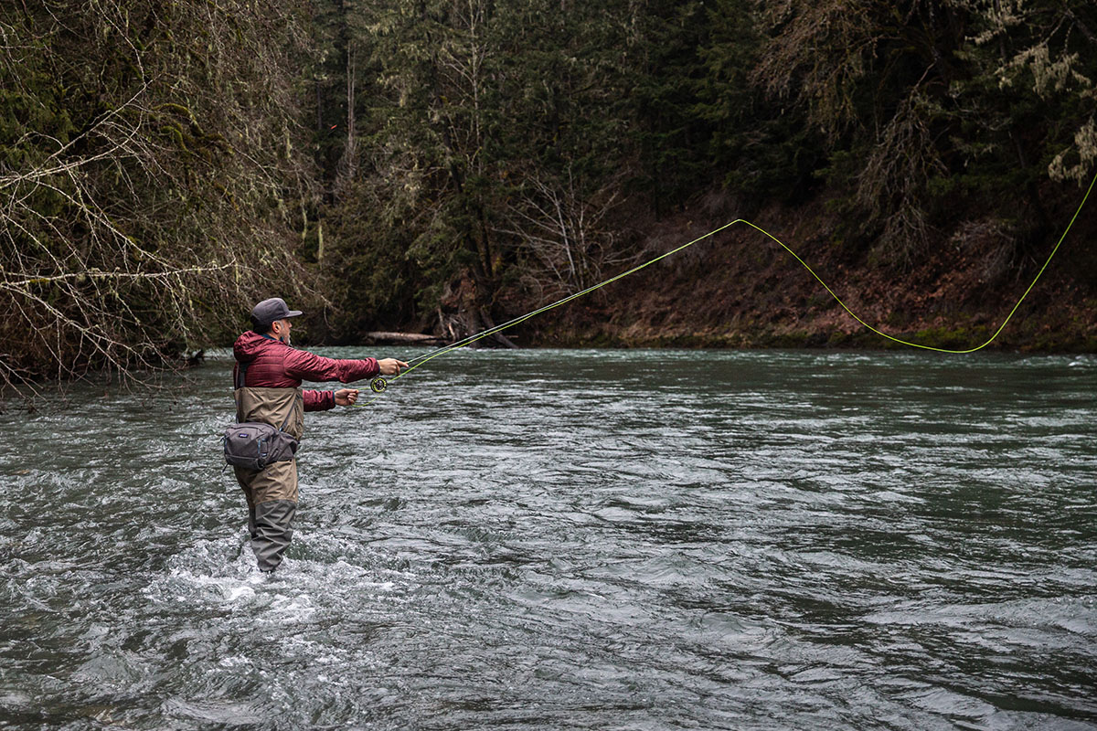 A fly fisherman wears a nanopuff hoody while casting in a mountain stream.