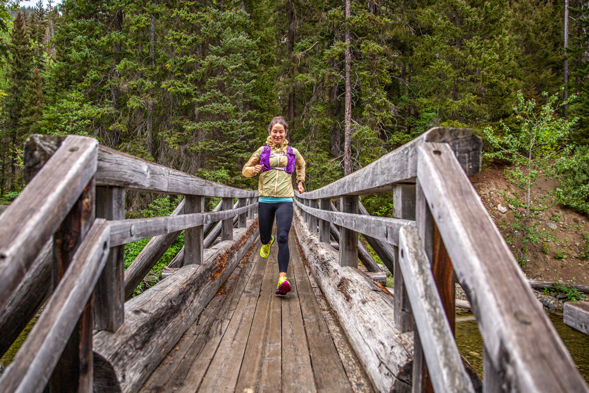 A woman runs over a wooden bridge in the forest.