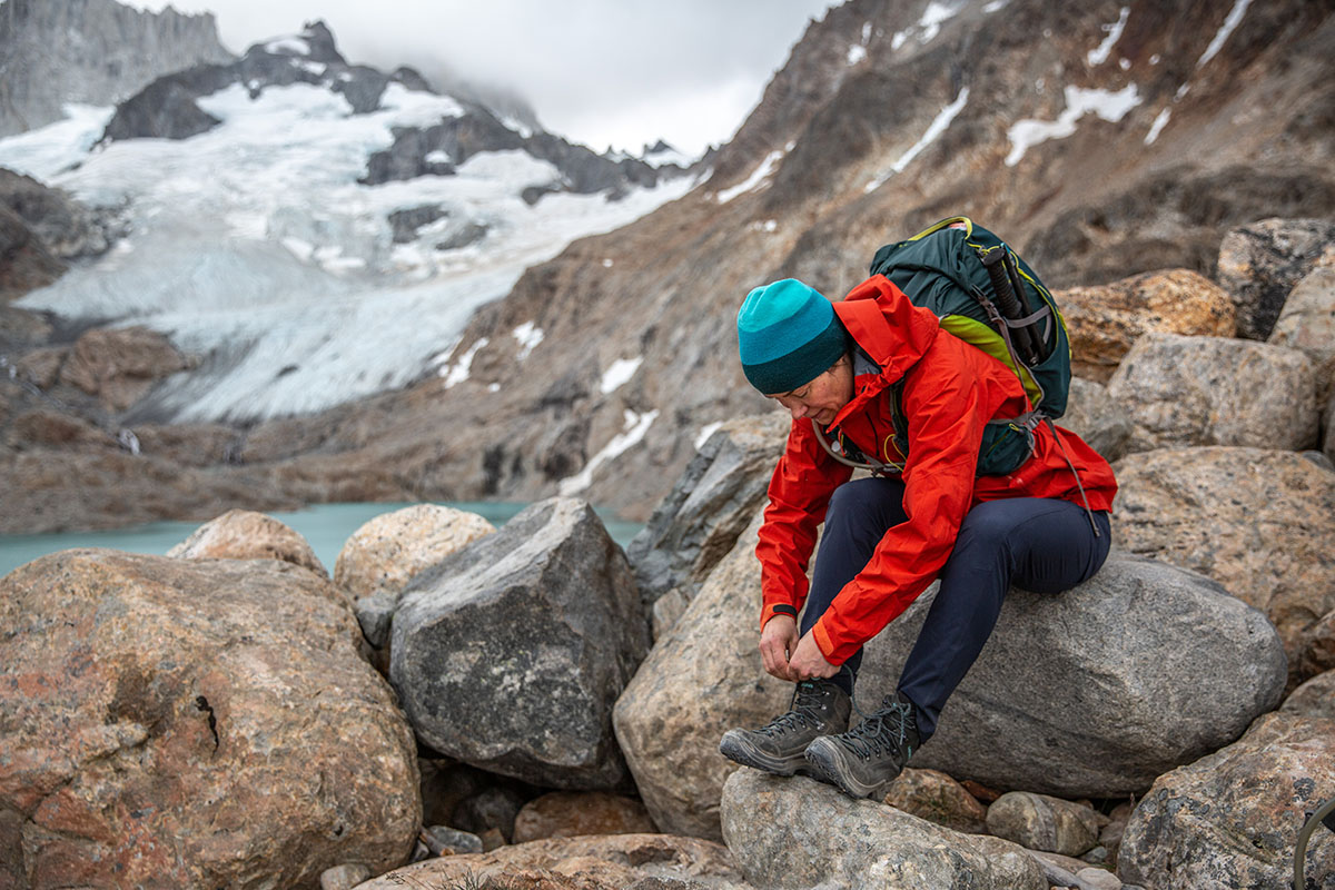 A woman sitting on a rock and tying black hiking boots