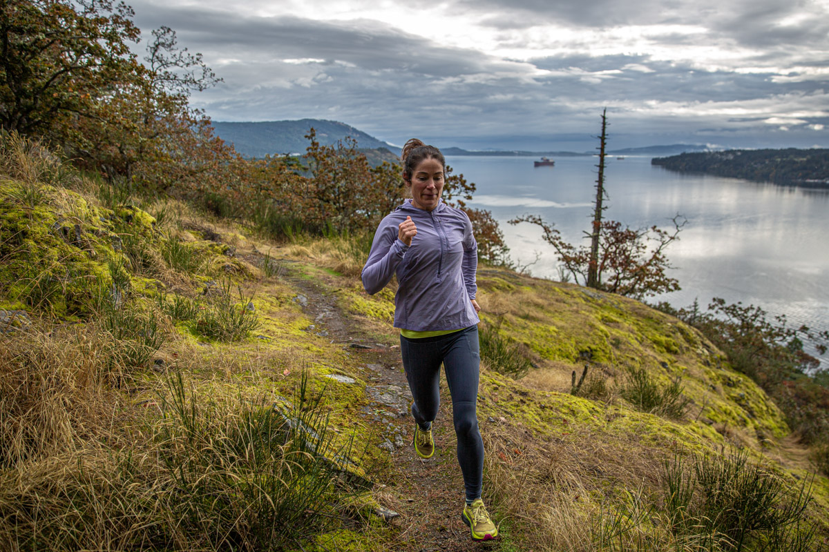 A woman trail running in a purple windbreaker