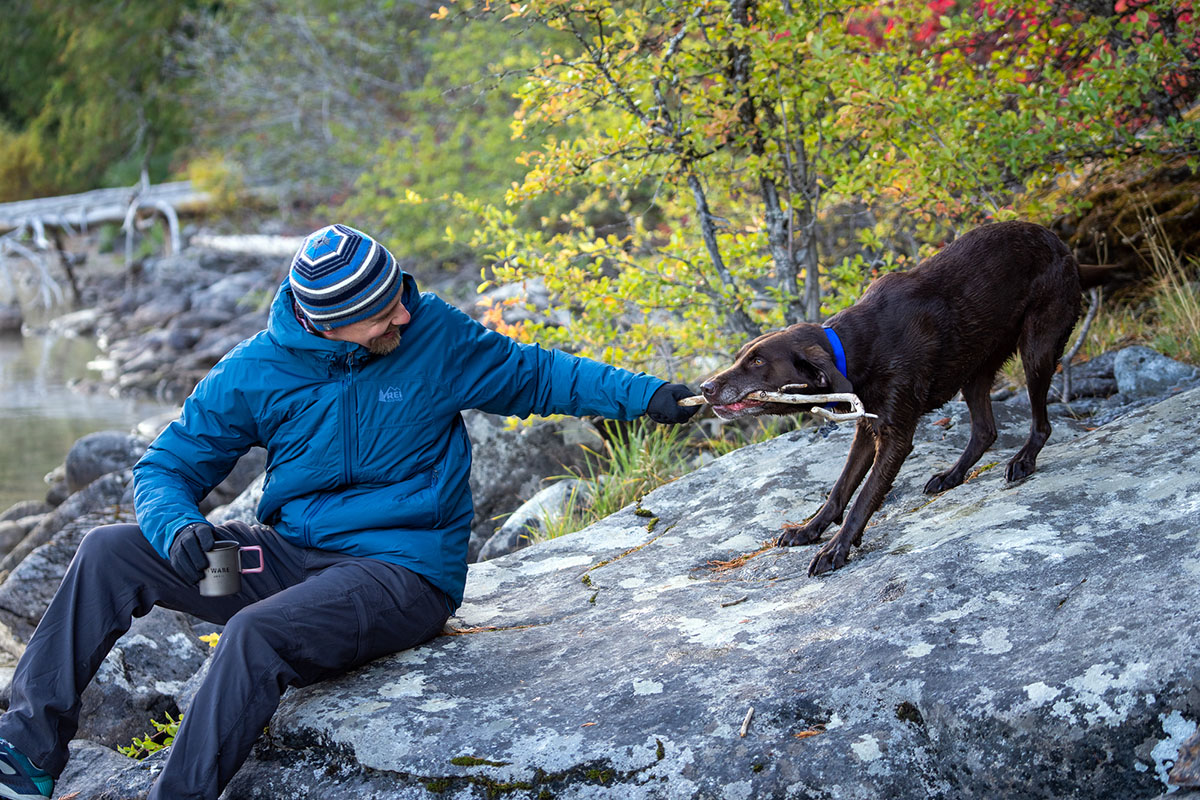 A man enjoys playing with his dog and having a cup of coffee outdoors.