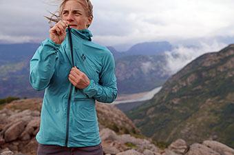 A woman stands in the wind and zips up a blue jacket