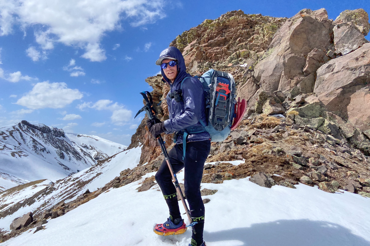 A man hiking in snow with a camera on his backpack strap
