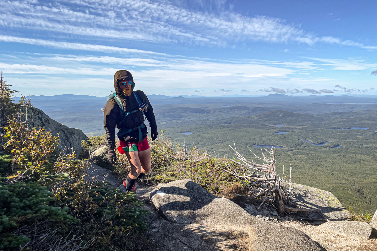 A man hiking on a trail with a camera on his backpack strap