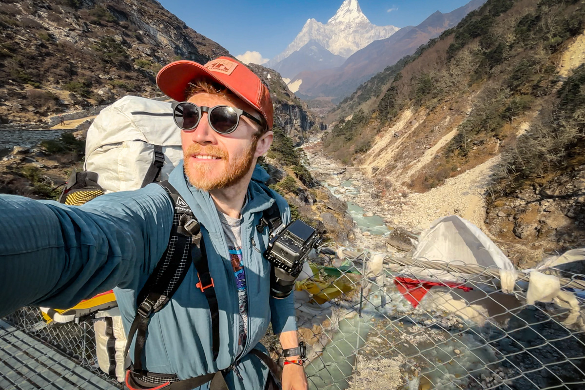A man hikes in Nepal with a Sony camera on his backpack strap