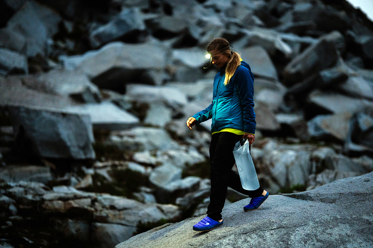 A woman walking across a rock in camp shoes