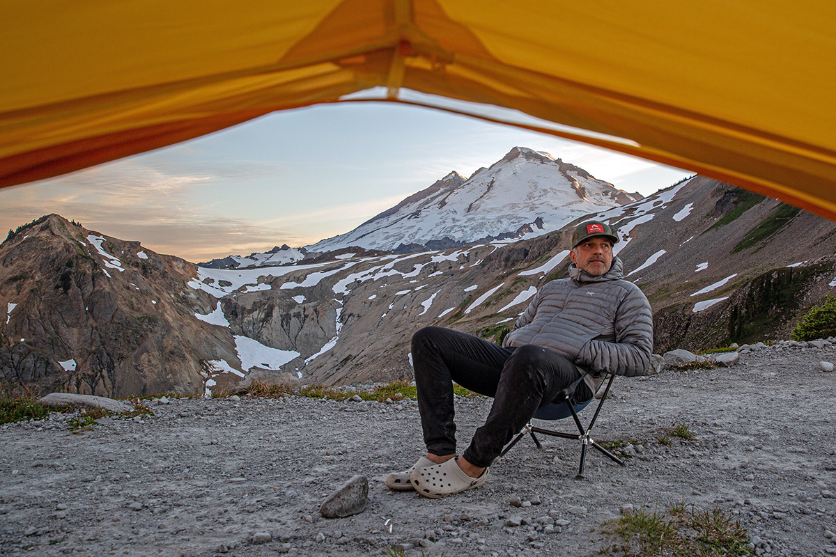 A man sitting outside a tent wearing camp shoes