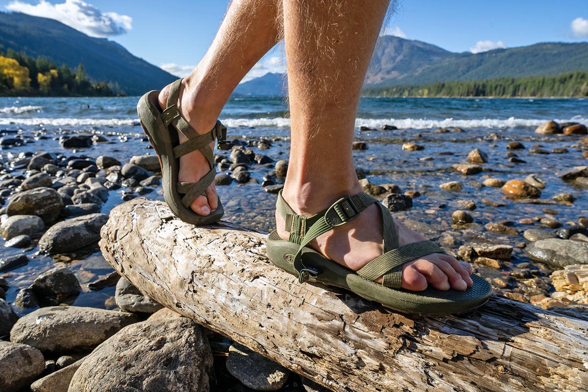 A close up of feet with Chaco sandals walking over a log