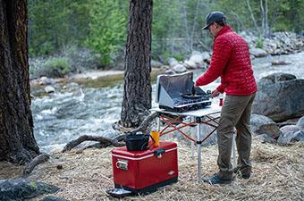 A camper sets up a cook stove at a wooded campground.