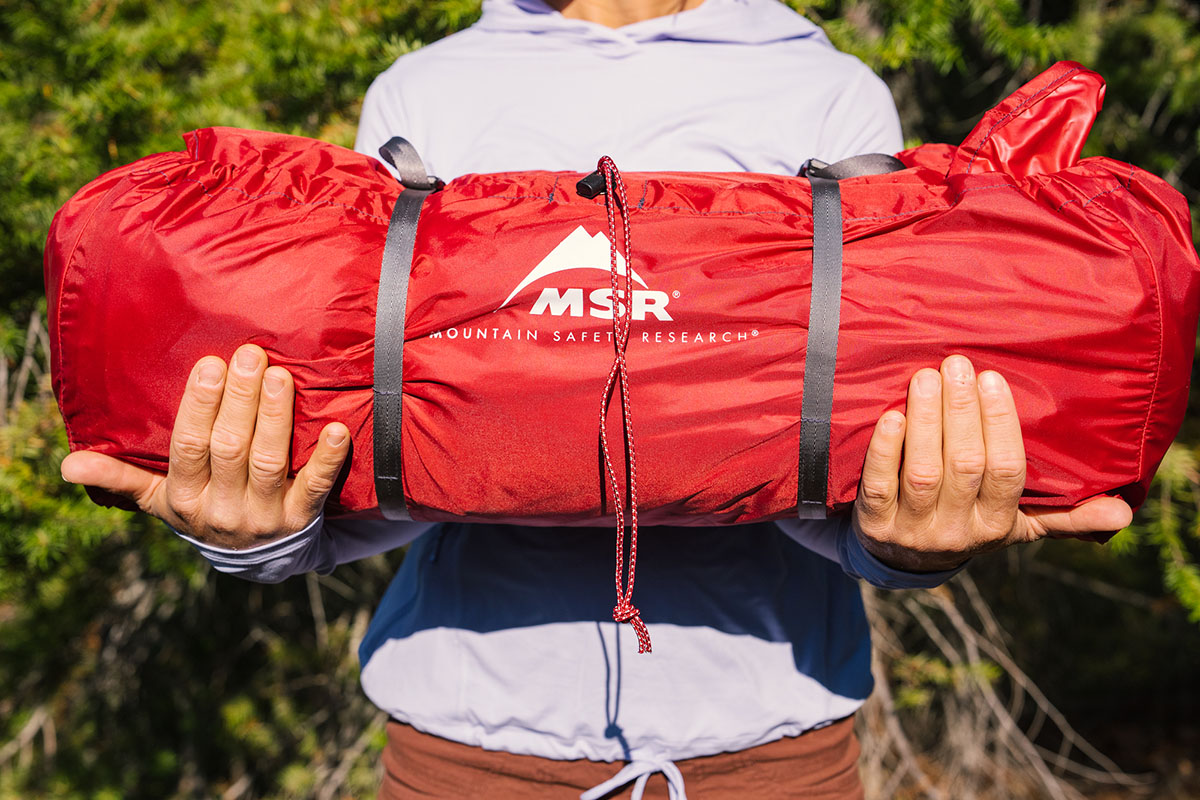 A camper holds up their camping tent, all rolled up into a neat package.