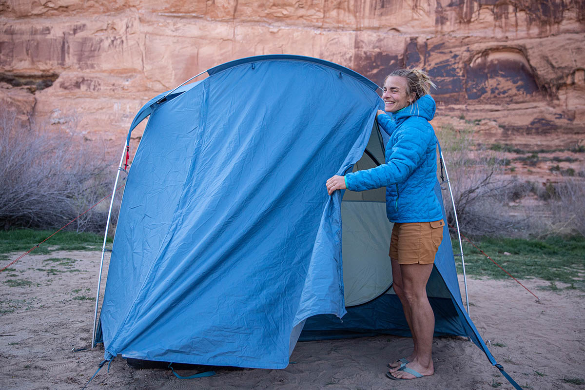 A woman smiles as she brushes aside the fly on her tent to get inside.