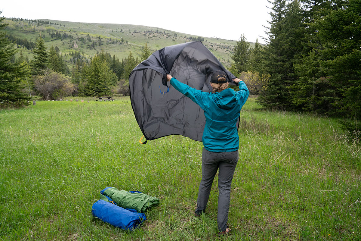 A camper begins setting up their tent by unfurling a footprint.