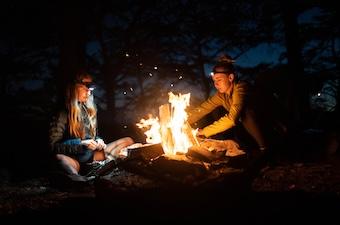 Two women sit in the dark around a large campfire