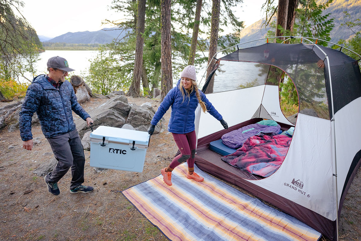 Two people carrying a cooler to a tent