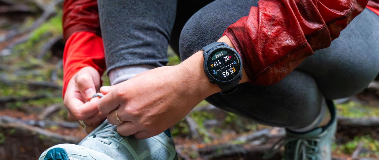 A hiker ties their shoelace, while showing off their Coros Pace 4 watch. 