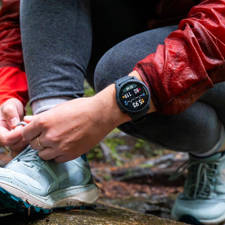 A hiker ties their shoelace, while showing off their Coros Pace 4 watch. 