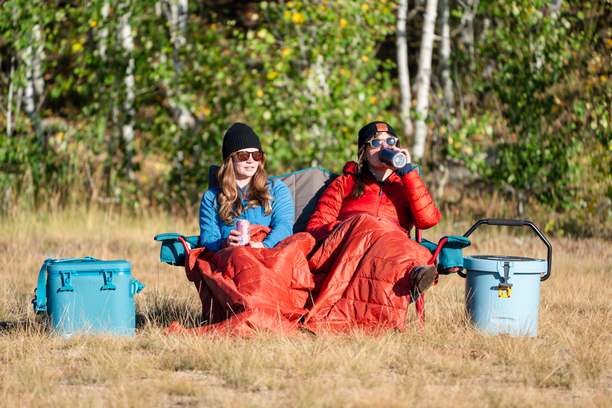 Two women sitting in a camping chair by coolers