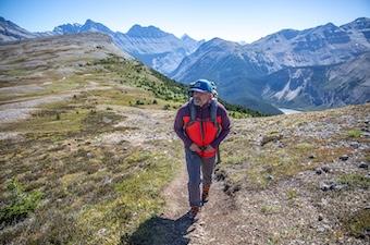 A man hikes on a mountain trail in a brightly colored fleece jacket