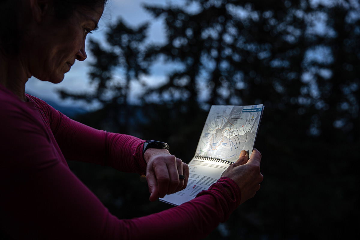 A woman using a flashlight on a GPS watch to look at a map