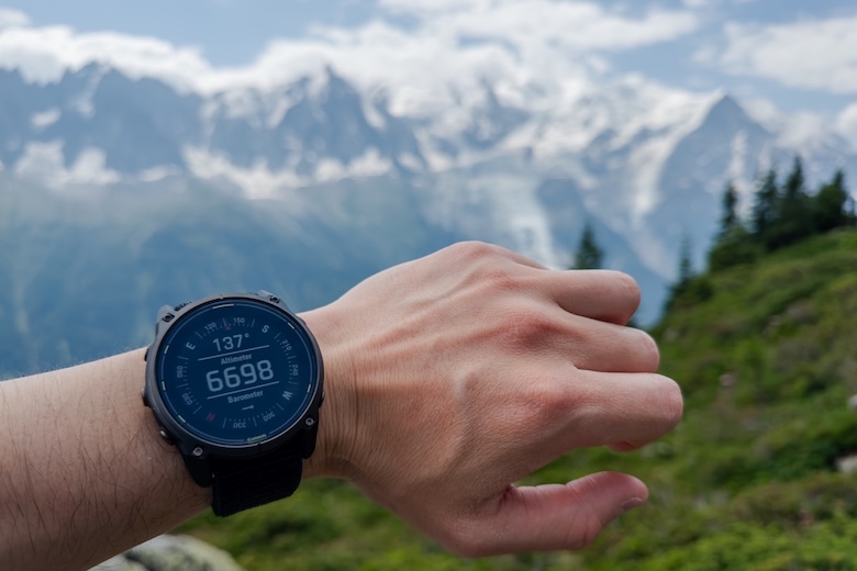 A wrist with a GPS watch is shown with mountains in the background