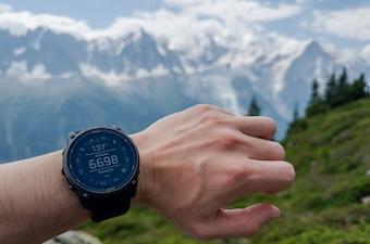 A wrist with a GPS watch is shown with mountains in the background