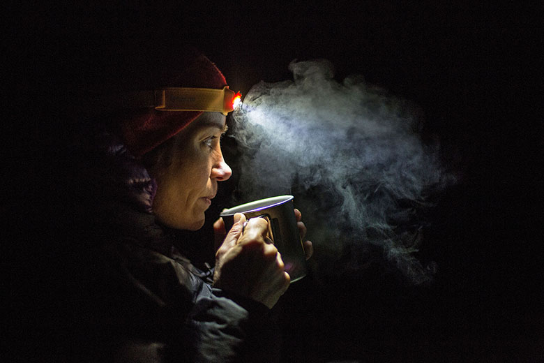 A woman drinking tea at night with her headlamp on