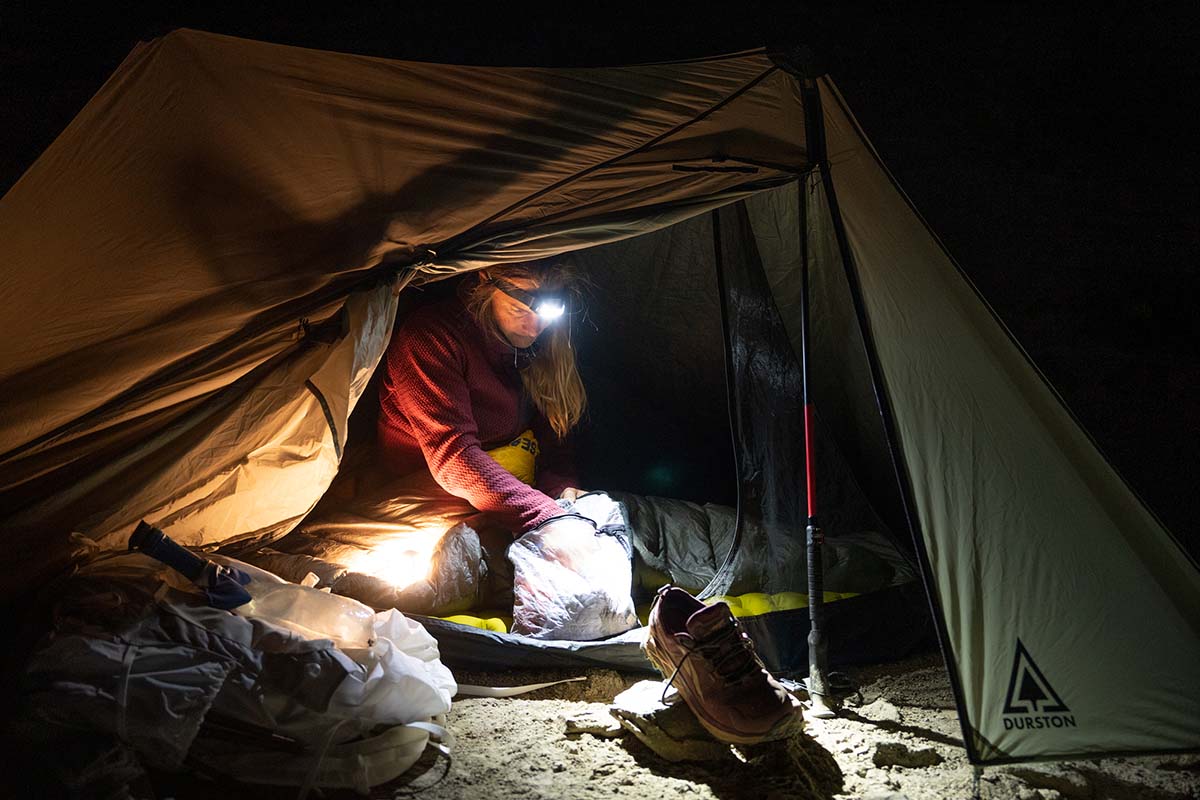 A woman organizing gear in a tent with a headlamp