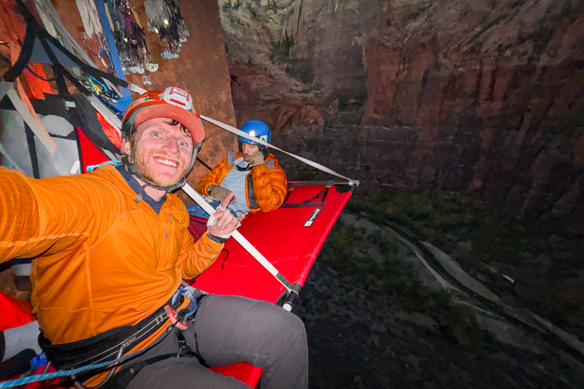 A man sitting on a portaledge with a headlamp on