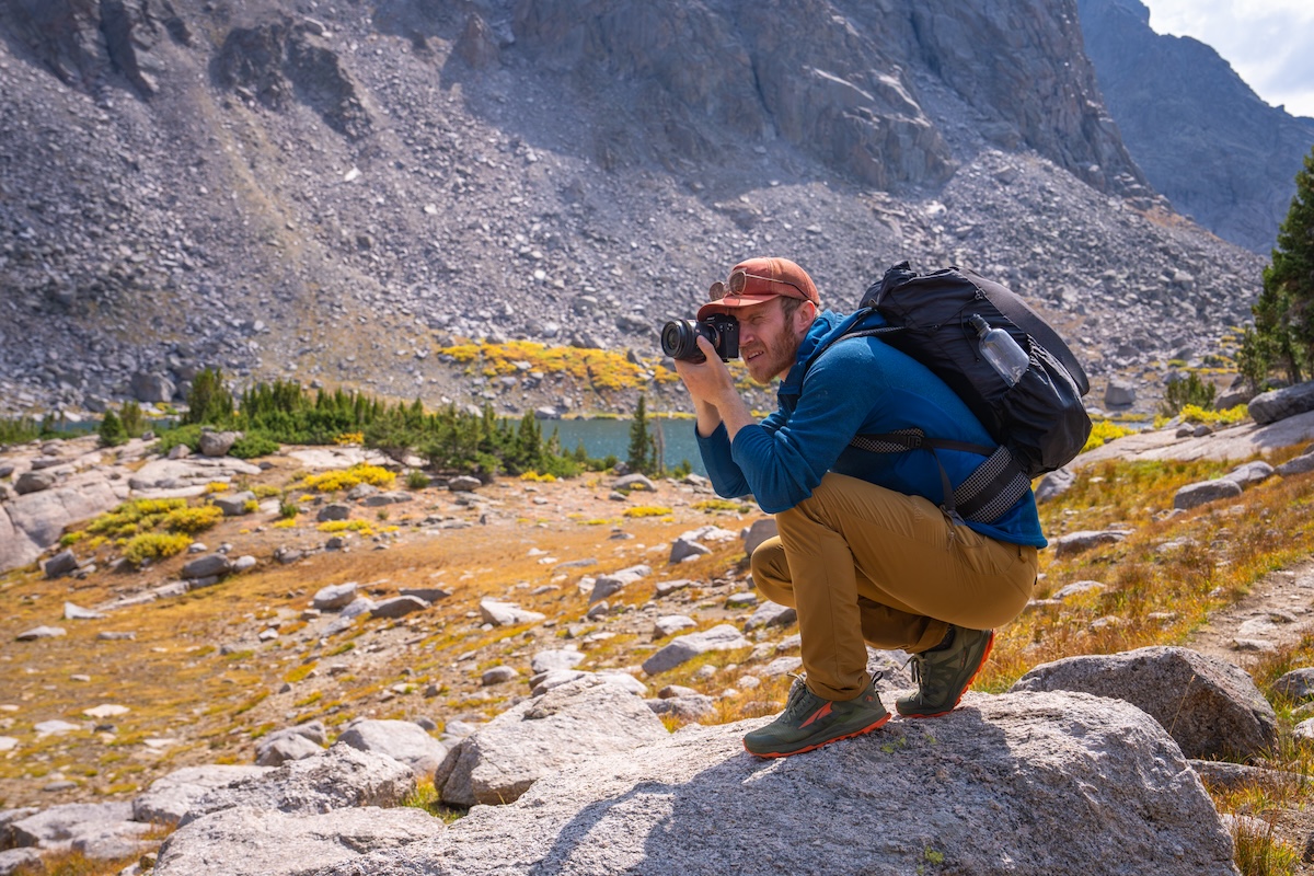 A hiker perches on a rock to take a photo.