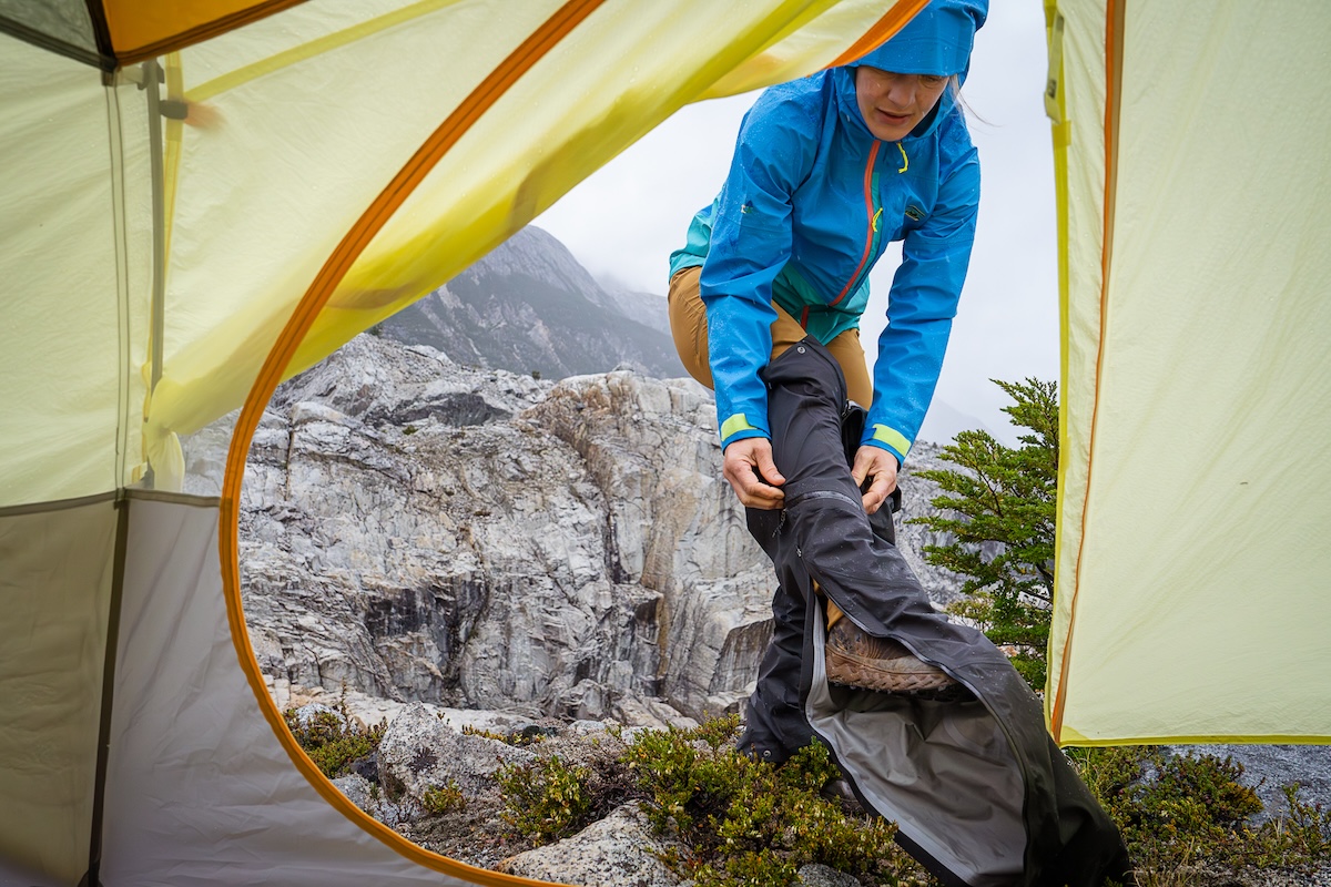 A hiker pulls on a pair of rain pants in wet weather.