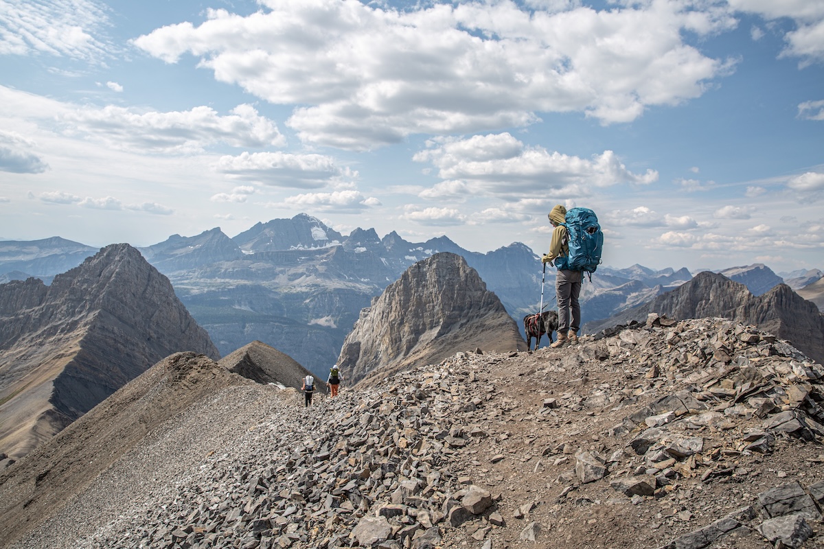 A woman hikes down a rocky slope with mountains in the background