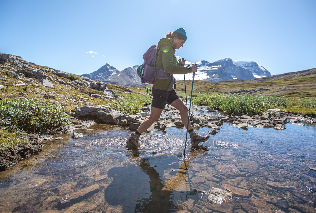 A woman crosses a stream in waterproof hiking boots