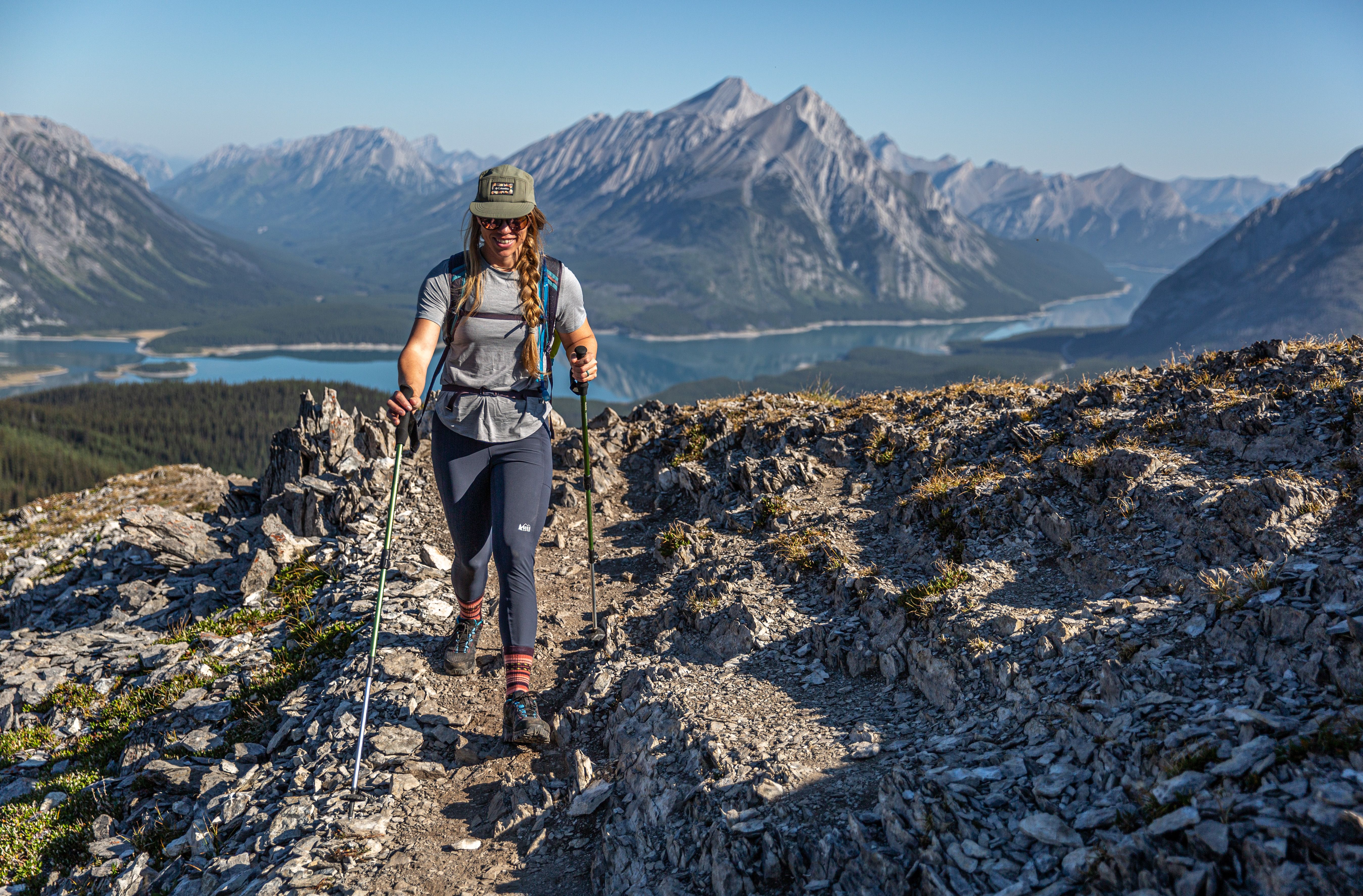 A hiker coms down a rocky path with a stunning mountain view in the background.