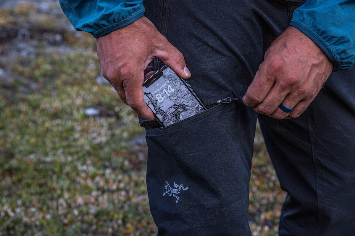 A hiker fits a cell phone into the thigh pocket of a pair of hiking pants.