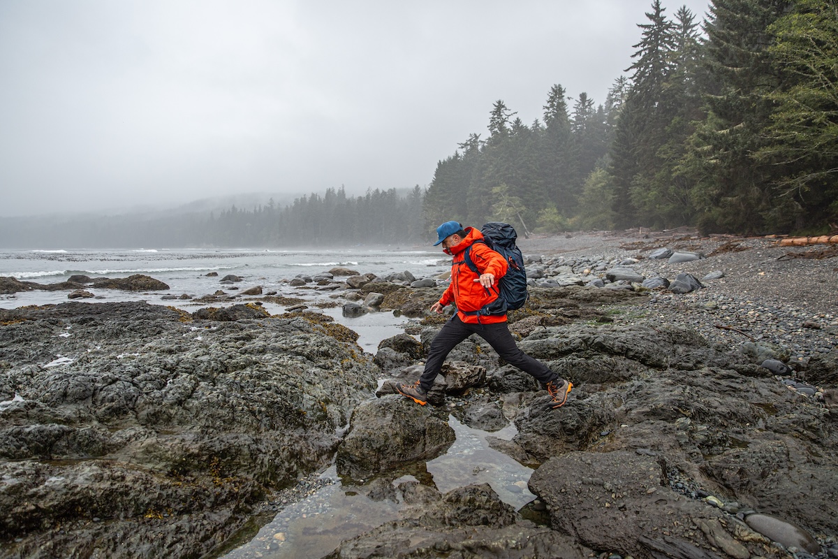 A hiker rock hops over a small stream.