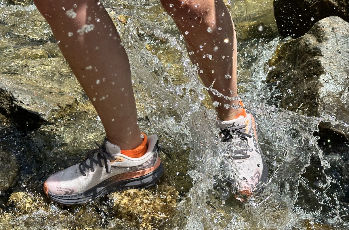A pair of Hoka shoes walking through a stream