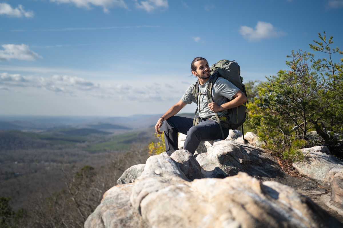 A hiker takes a break by sitting on a rock.