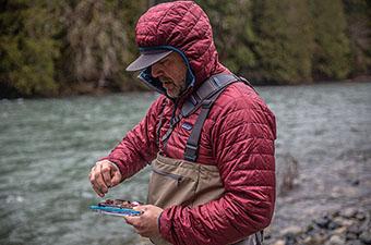 A fly fisher looks for a fly while wearing the Patagonia Nano Puff hoody to keep warm. 
