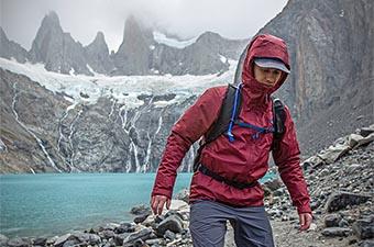 A man in a rain jacket hiking by alpine lake