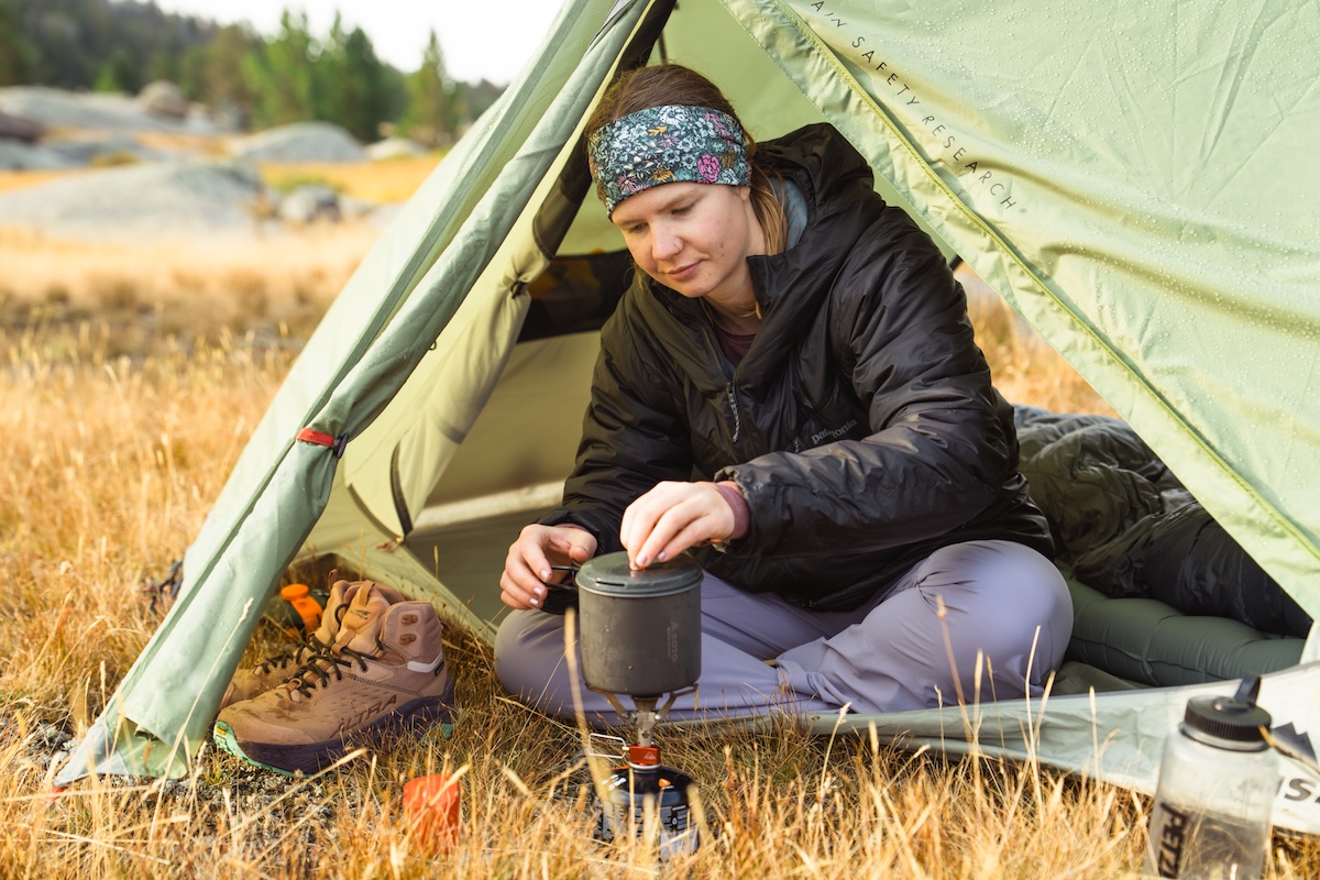 A woman making coffee in tent wearing synthetic jacket