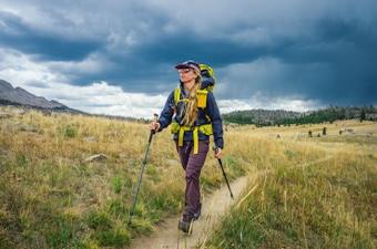 A woman in an Arc'teryx rain jacket hikes in front of ominous clouds in Wyoming