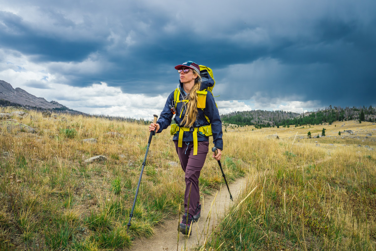 A woman in an Arc'teryx rain jacket hikes in front of ominous clouds in Wyoming