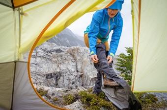 A woman pulling on rain pants outside a tent