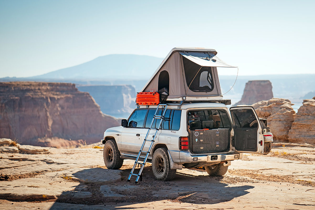 A car parked overlooking a great canyon with pillars and mesas, with a rooftop tent opened up on top.