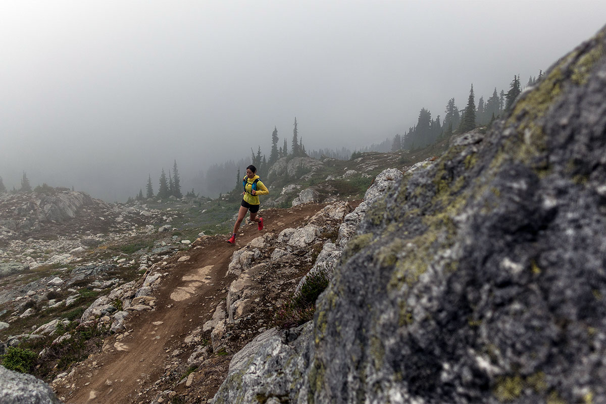A trail runner runs along a ridge in rainy mountains.