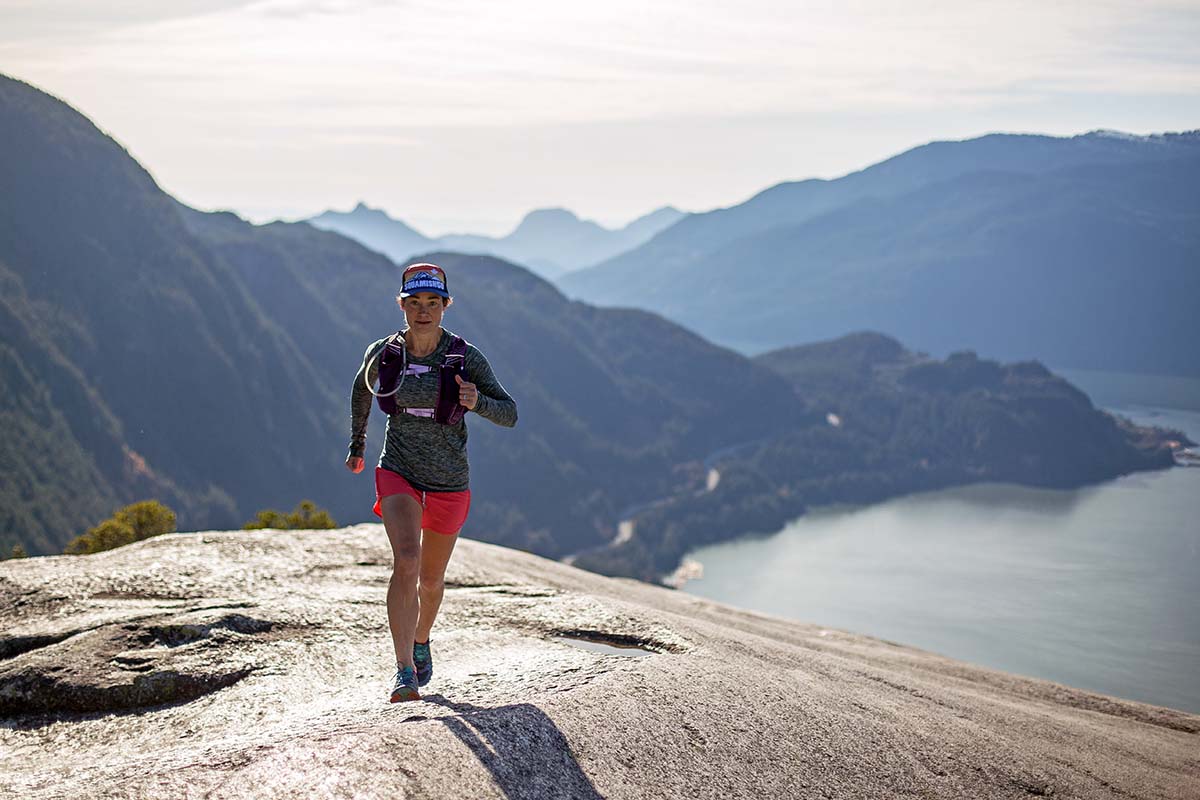 A runner climbs a smooth rock on a trail high above an alpine lake.