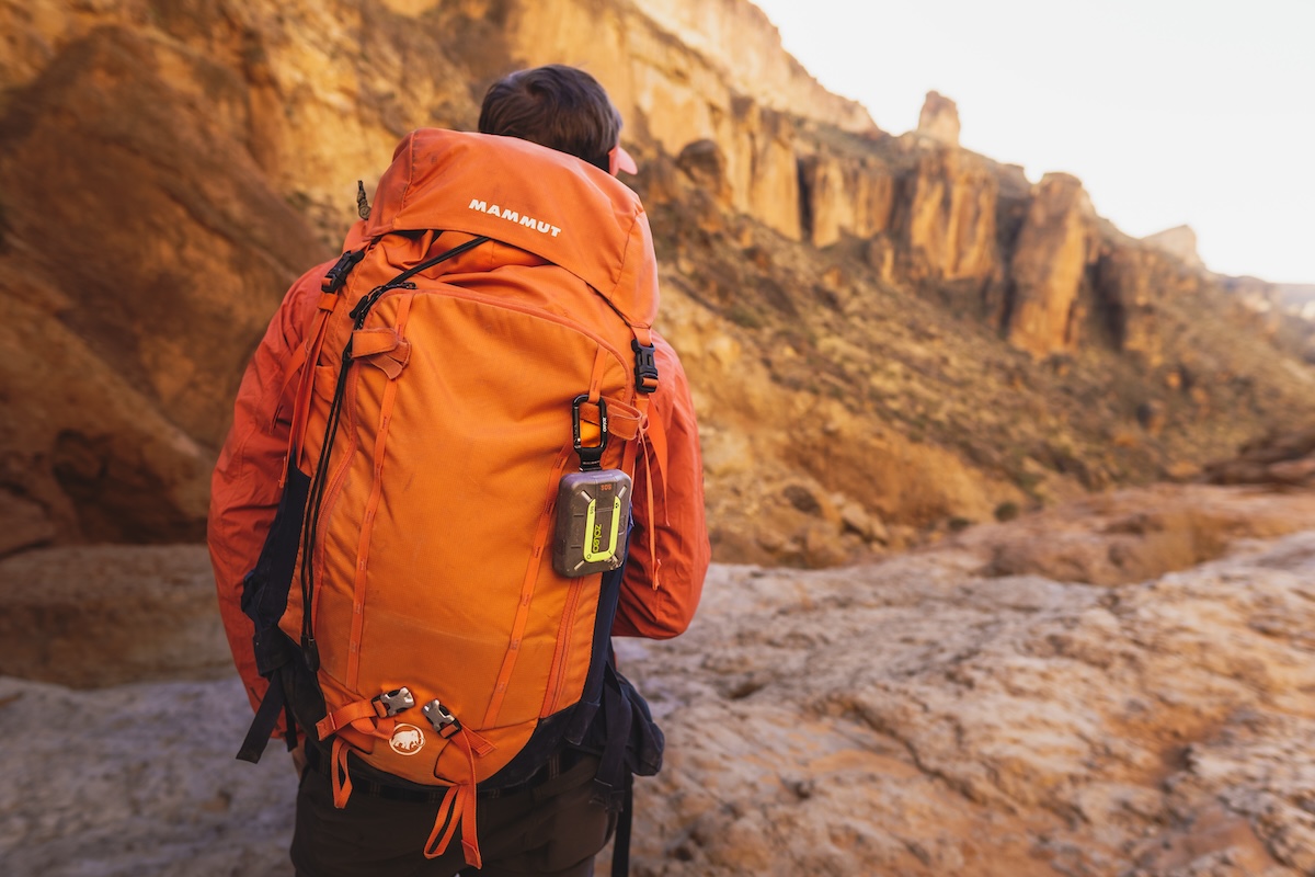 A large orange backpack with the Zoleo messenger attached via a carabiner