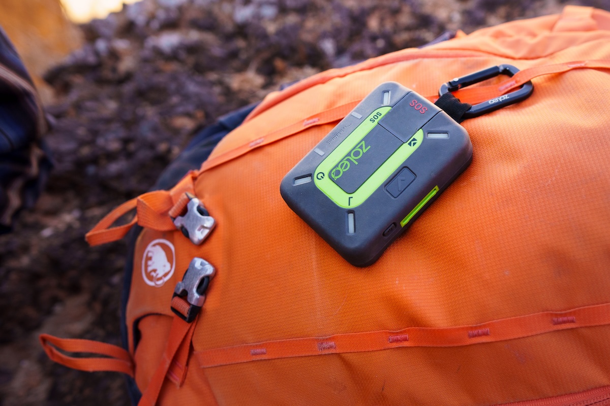A close up of the Zoleo communicator clipped to an orange backpack