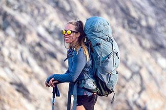 A woman smiles while hauling a backpacking pack through the wilderness