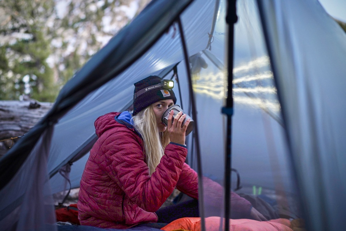 A camper has a warm drink in her tent while bundled up on a fall day.